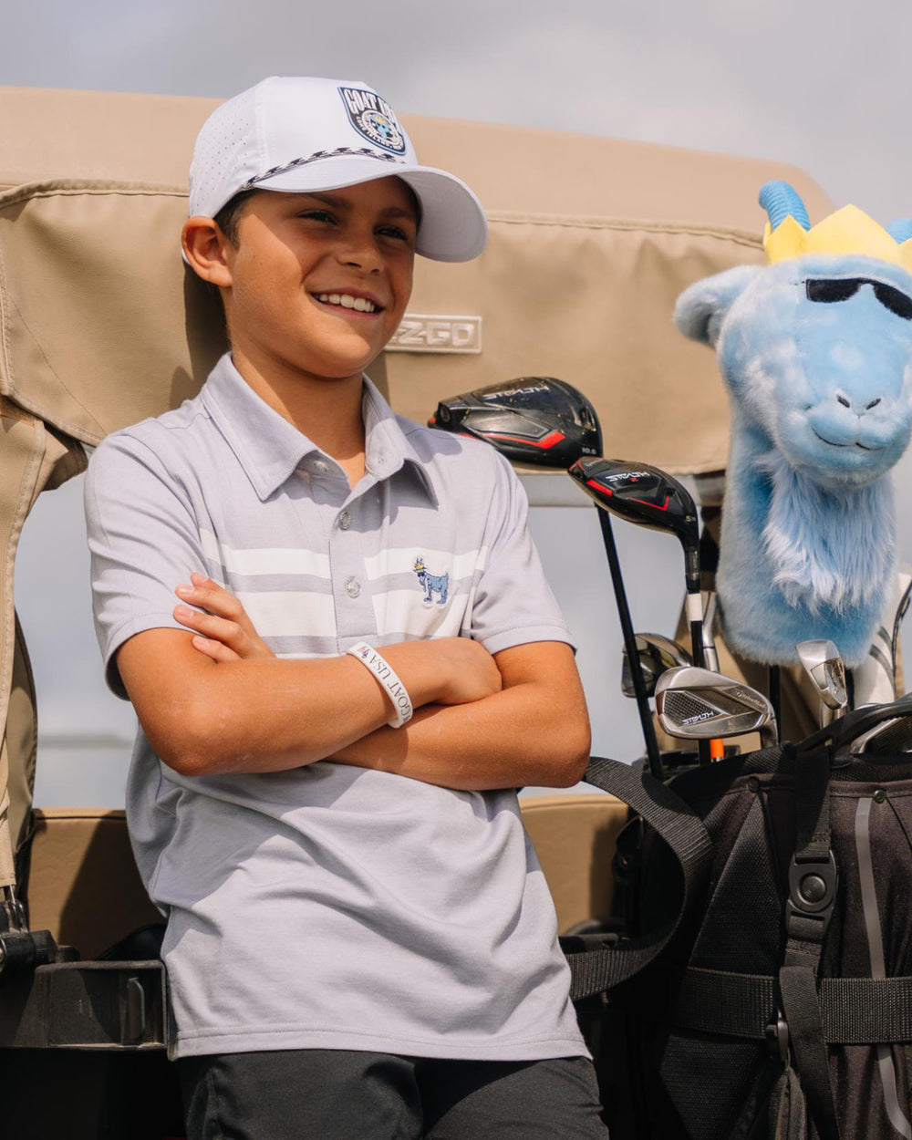 Kid with arms crossed leaning on a golf cart#color_gray