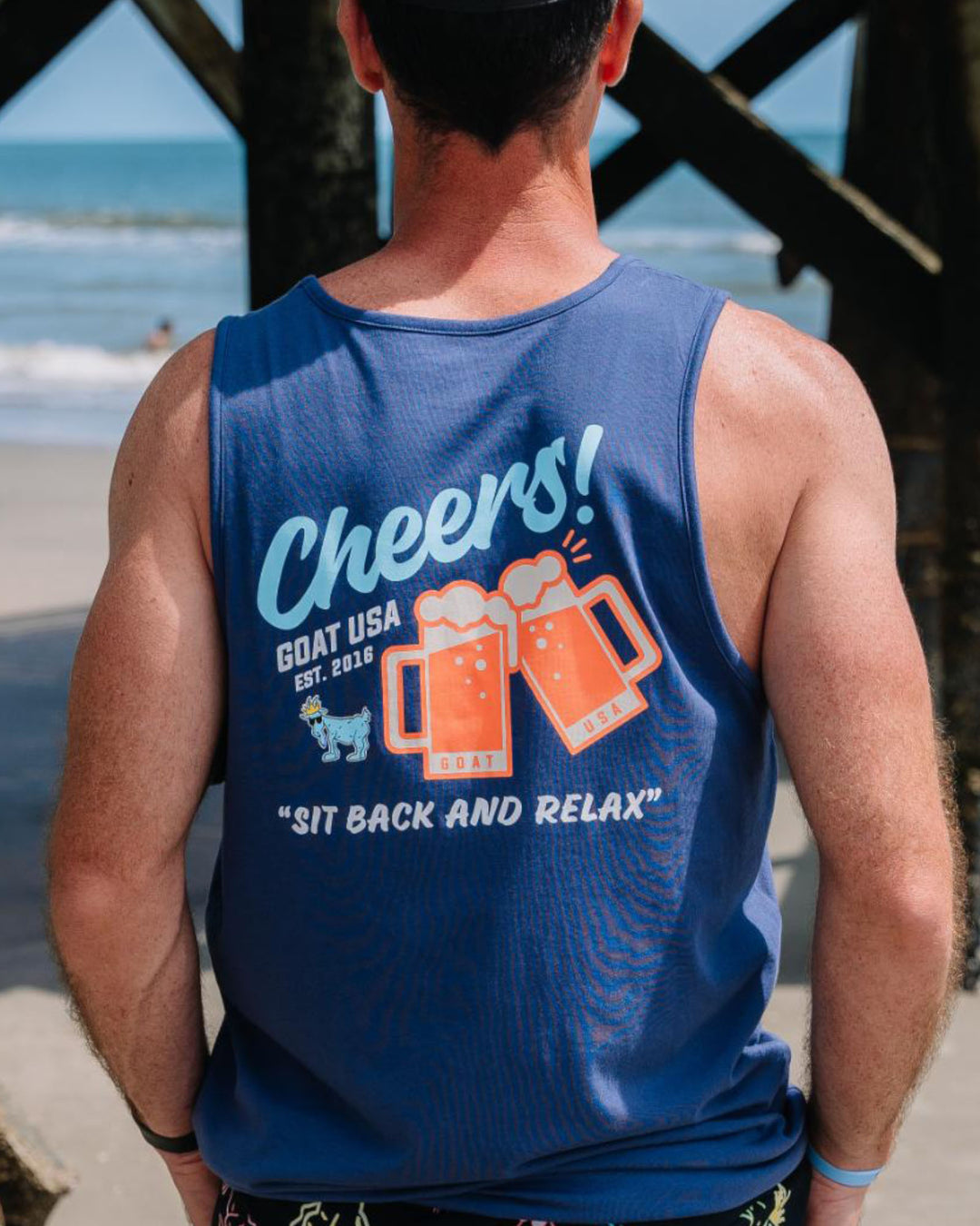 Man on the beach facing the boardwalk, photo is zoomed in on navy tank top